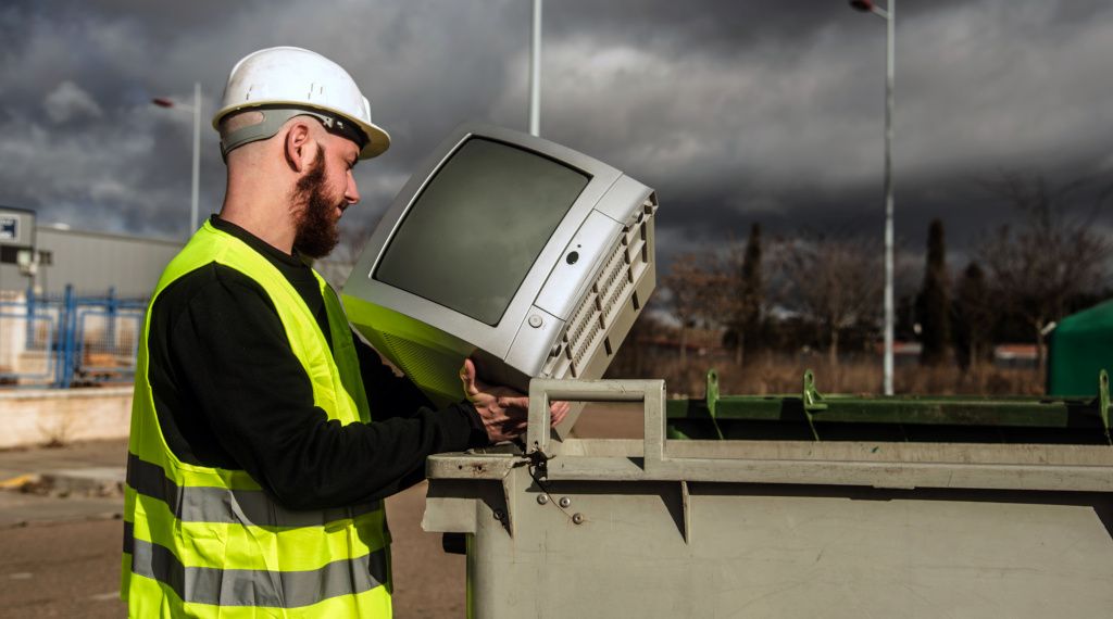 Recycling operative wearing high-vis vest is placing old box tv into recycling bin